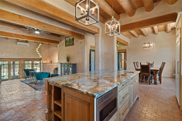 kitchen with sink, decorative light fixtures, a chandelier, stainless steel microwave, and a kitchen island with sink