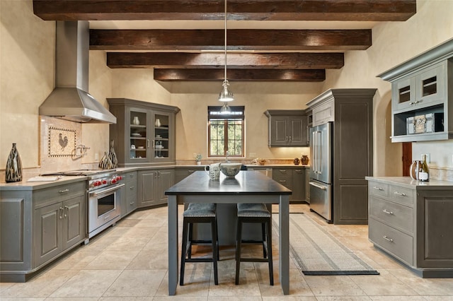 kitchen with premium appliances, wall chimney range hood, hanging light fixtures, beamed ceiling, and gray cabinets