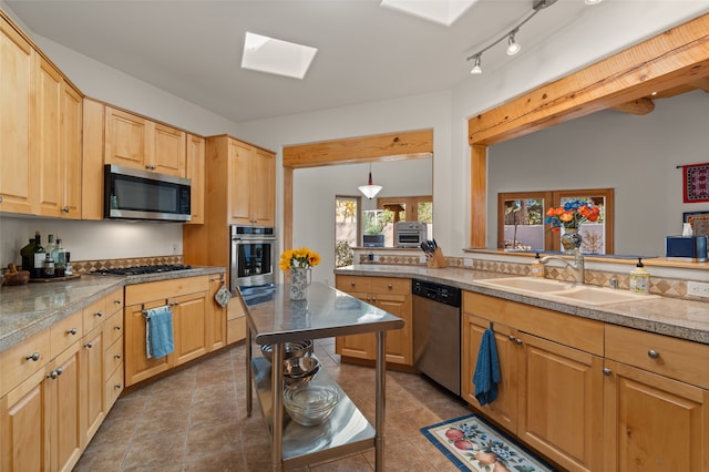 kitchen featuring stainless steel appliances, sink, a skylight, light brown cabinetry, and decorative light fixtures