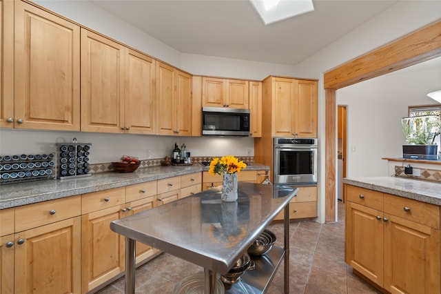 kitchen featuring stainless steel appliances, light brown cabinetry, and dark tile patterned flooring