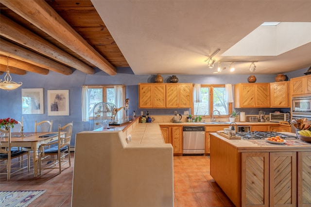 kitchen with light brown cabinetry, stainless steel appliances, sink, light tile patterned floors, and beamed ceiling