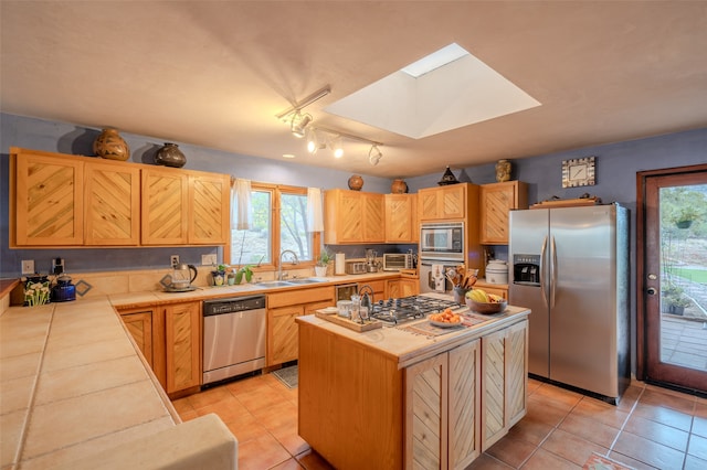 kitchen with a skylight, stainless steel appliances, sink, light tile patterned floors, and a center island