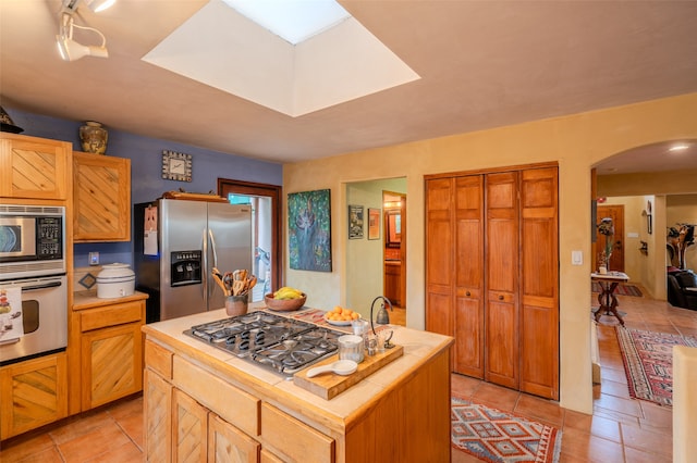 kitchen with a center island with sink, light tile patterned floors, and stainless steel appliances