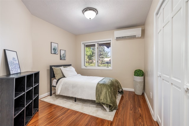 bedroom with a closet, a textured ceiling, dark hardwood / wood-style flooring, and a wall mounted air conditioner