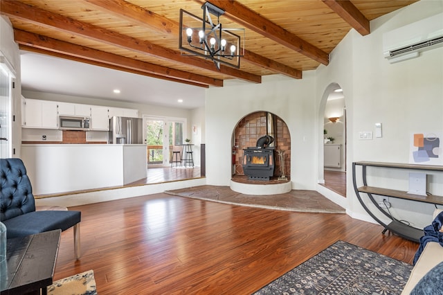 living room with dark hardwood / wood-style floors, an AC wall unit, beam ceiling, a wood stove, and wooden ceiling