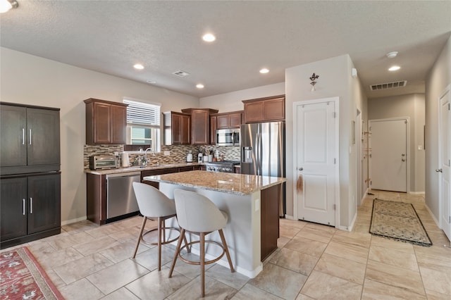 kitchen featuring tasteful backsplash, a kitchen island, appliances with stainless steel finishes, a kitchen breakfast bar, and light stone counters