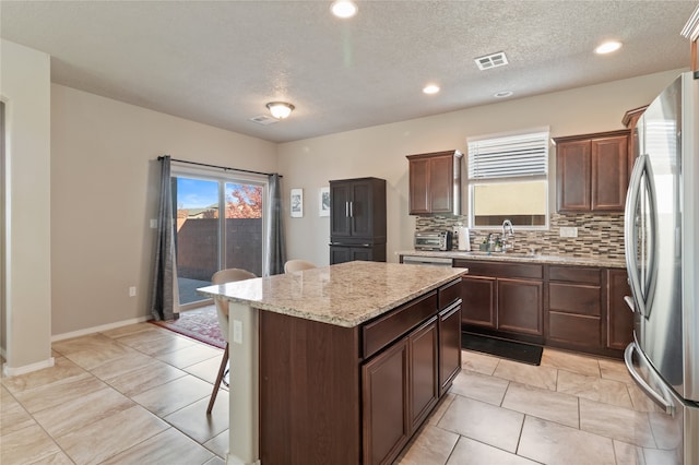 kitchen with sink, backsplash, a textured ceiling, a center island, and stainless steel fridge