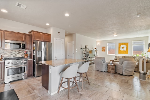 kitchen with tasteful backsplash, appliances with stainless steel finishes, a kitchen bar, a center island, and light stone counters