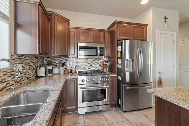 kitchen featuring tasteful backsplash, appliances with stainless steel finishes, a textured ceiling, light stone countertops, and sink