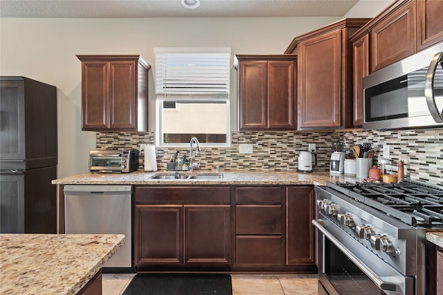 kitchen with decorative backsplash, light tile patterned floors, appliances with stainless steel finishes, light stone countertops, and sink