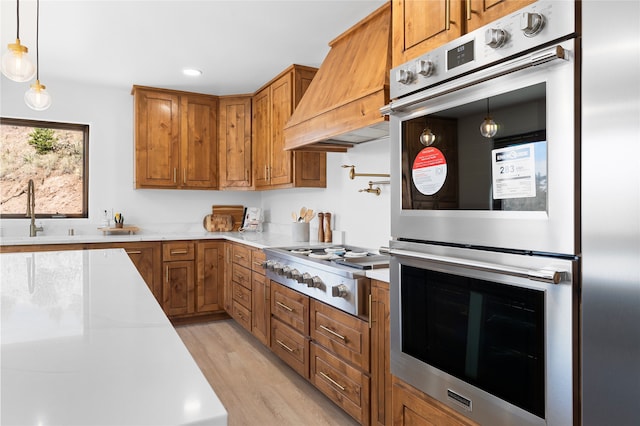 kitchen featuring appliances with stainless steel finishes, light wood-type flooring, custom range hood, sink, and decorative light fixtures