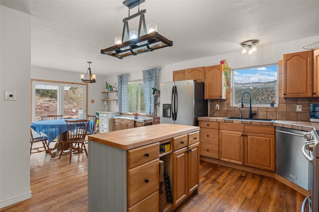 kitchen with sink, appliances with stainless steel finishes, dark hardwood / wood-style floors, decorative light fixtures, and a center island