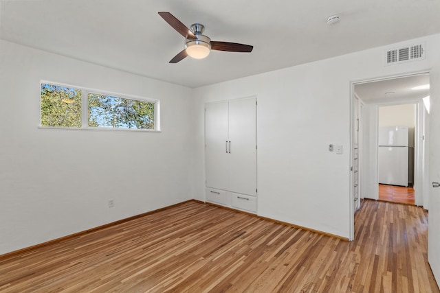 unfurnished bedroom featuring a closet, ceiling fan, light hardwood / wood-style flooring, and refrigerator