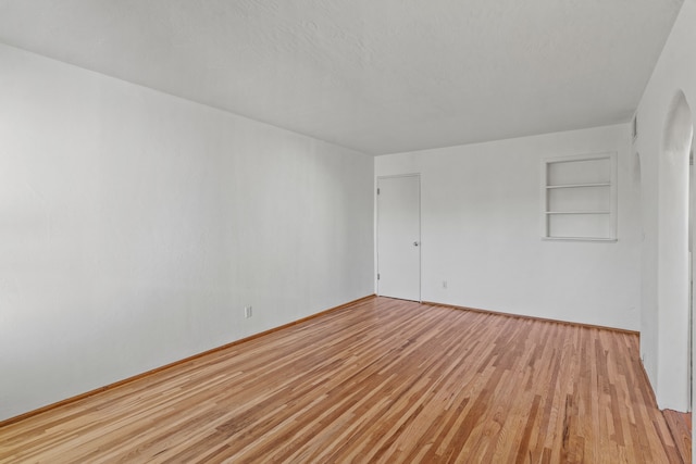 unfurnished room with built in shelves and light wood-type flooring