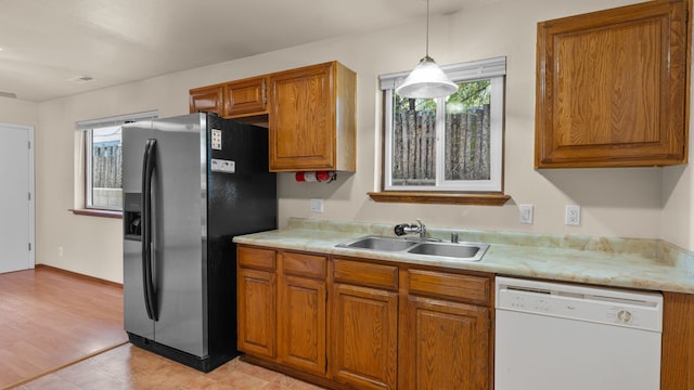 kitchen featuring sink, hanging light fixtures, stainless steel fridge, white dishwasher, and light wood-type flooring