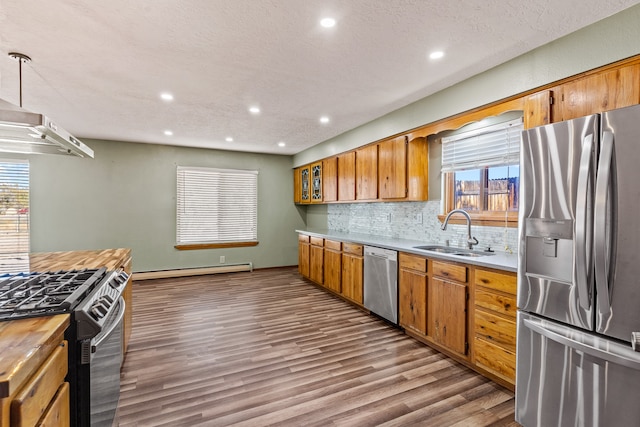 kitchen with pendant lighting, sink, hardwood / wood-style flooring, appliances with stainless steel finishes, and a baseboard radiator