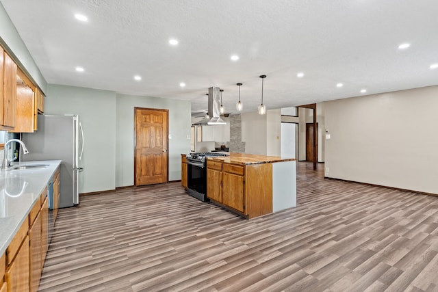 kitchen featuring pendant lighting, ventilation hood, sink, light hardwood / wood-style flooring, and stainless steel gas range