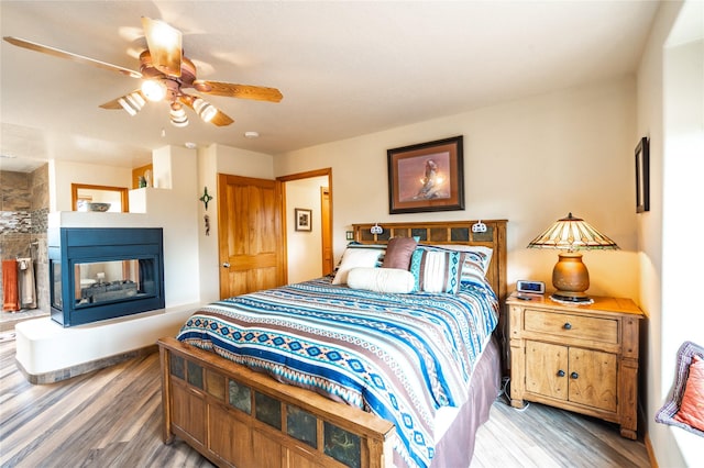 bedroom with ceiling fan, a multi sided fireplace, and hardwood / wood-style floors