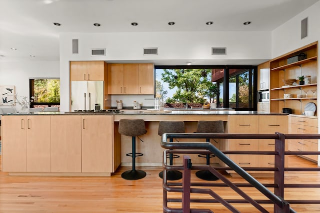 kitchen featuring light brown cabinetry, built in appliances, a healthy amount of sunlight, and light wood-type flooring