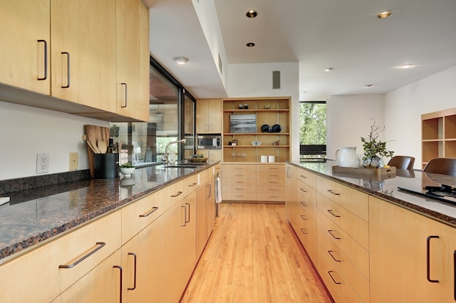 kitchen featuring dark stone counters, light brown cabinetry, sink, and light hardwood / wood-style flooring