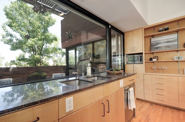 kitchen featuring stainless steel appliances, light brown cabinets, sink, light hardwood / wood-style floors, and dark stone countertops