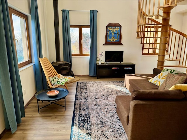 living area featuring stairs, a wood stove, baseboards, and wood finished floors