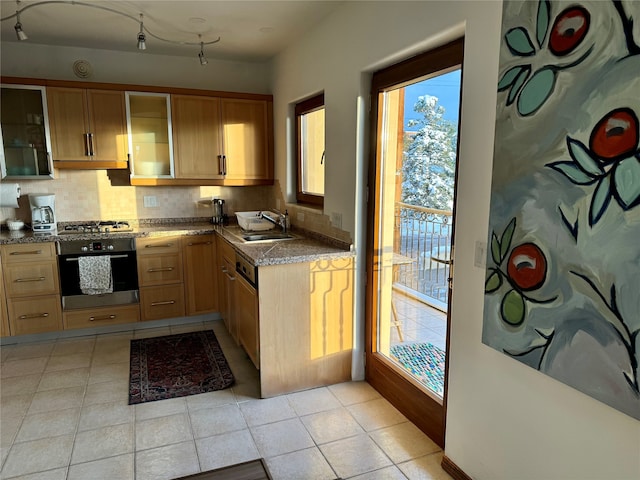 kitchen featuring tasteful backsplash, stainless steel appliances, light tile patterned floors, sink, and dark stone countertops