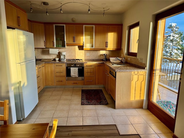 kitchen with glass insert cabinets, decorative backsplash, appliances with stainless steel finishes, light tile patterned flooring, and a sink