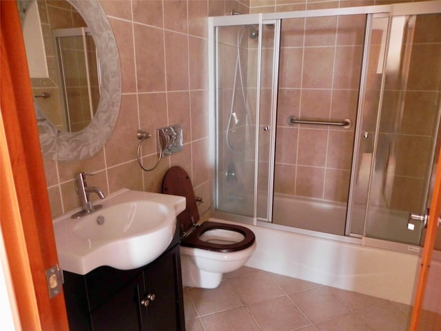 bathroom with vanity, bath / shower combo with glass door, tile patterned floors, toilet, and tile walls