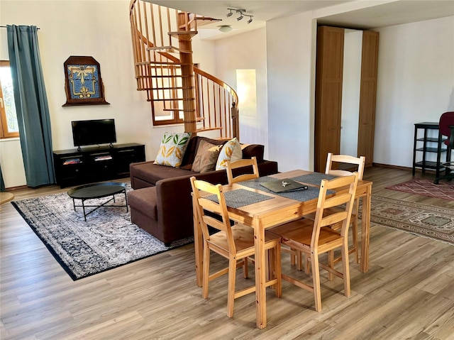 dining room with stairway, rail lighting, light wood-type flooring, and baseboards