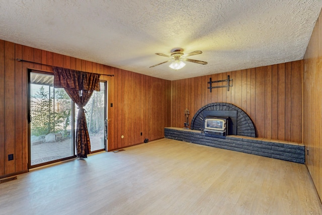 2709 Paseo De Tularosa, Santa Fe, NM 87505 - unfurnished living room featuring a textured ceiling, a wood stove, wooden walls, ceiling fan, and light hardwood / wood-style flooring
