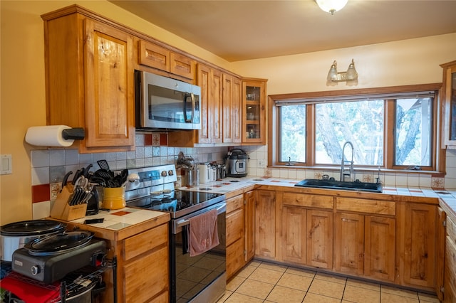 kitchen with tile countertops, decorative backsplash, sink, light tile patterned floors, and appliances with stainless steel finishes