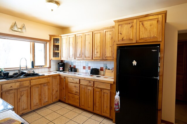 kitchen with tile counters, black fridge, sink, tasteful backsplash, and light tile patterned floors