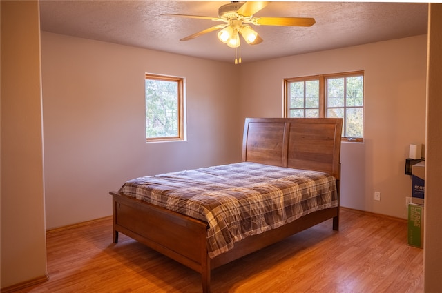 bedroom featuring a textured ceiling, light hardwood / wood-style flooring, multiple windows, and ceiling fan