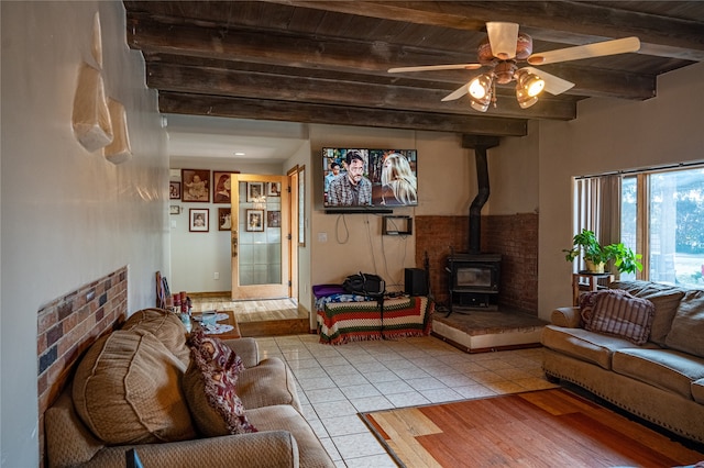 living room with beam ceiling, light tile patterned floors, a wood stove, and wood ceiling