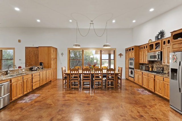 kitchen with appliances with stainless steel finishes, concrete floors, light stone counters, and hanging light fixtures