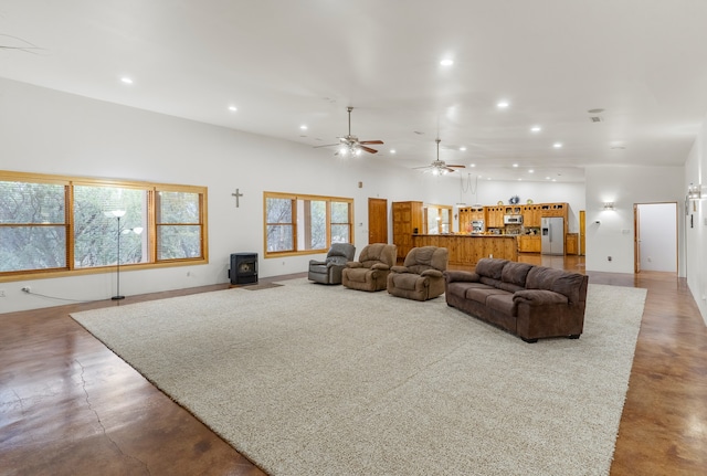 living room with concrete flooring, a wood stove, ceiling fan, and a towering ceiling