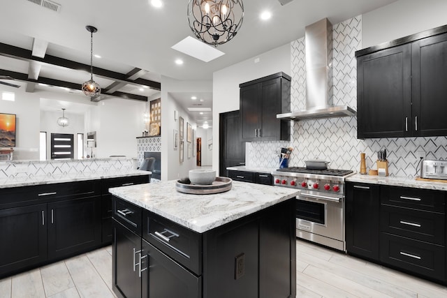 kitchen featuring premium stove, beam ceiling, backsplash, a kitchen island, and wall chimney range hood