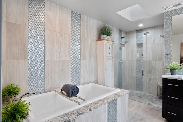 bathroom featuring independent shower and bath, vanity, a skylight, and tile walls