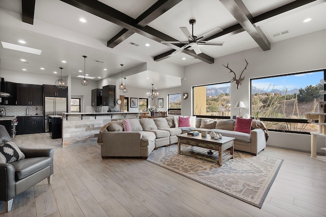 living room featuring light wood-type flooring, coffered ceiling, ceiling fan with notable chandelier, and beamed ceiling