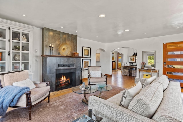 living room with arched walkways, recessed lighting, a tiled fireplace, and wood finished floors