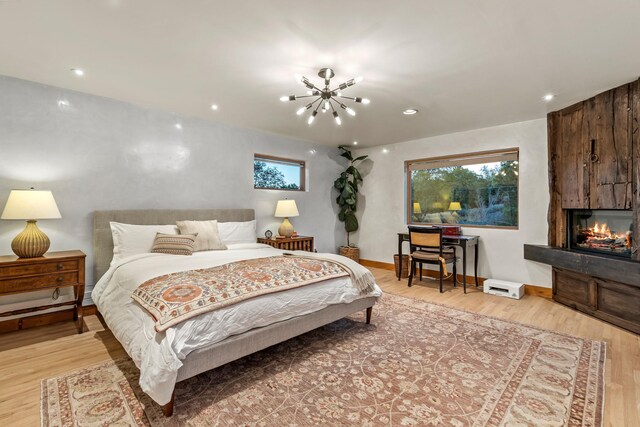 bedroom featuring a chandelier, a fireplace, light wood-style flooring, and baseboards