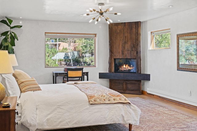 bedroom featuring light wood-type flooring, a baseboard radiator, baseboards, and a notable chandelier