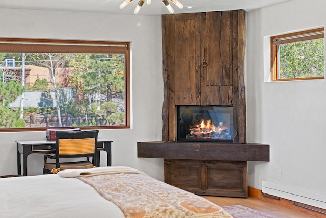 bedroom with light wood finished floors, baseboard heating, a glass covered fireplace, and baseboards