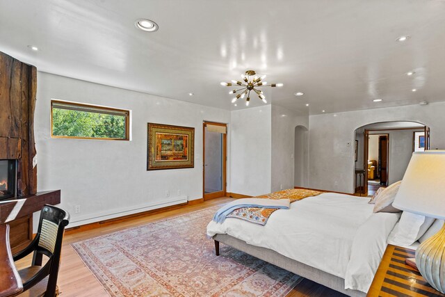 bedroom featuring a fireplace, a baseboard radiator, a notable chandelier, and light wood-type flooring