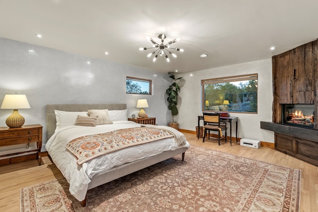 bedroom with a large fireplace, an inviting chandelier, and light hardwood / wood-style flooring