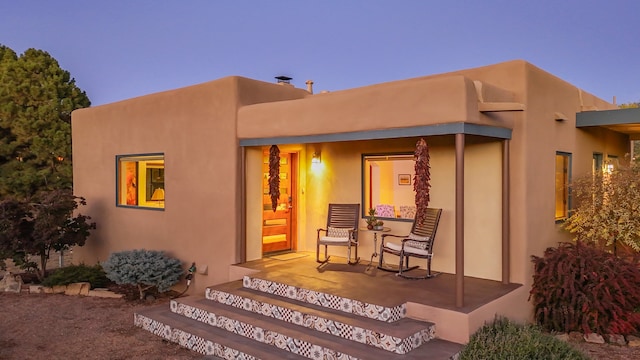 back house at dusk featuring a porch