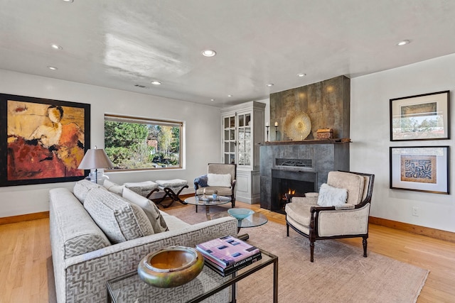 living room featuring light wood-type flooring, a fireplace, baseboards, and recessed lighting