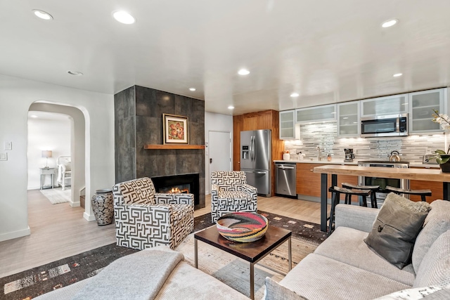 living area featuring light wood-style floors, a fireplace, arched walkways, and recessed lighting