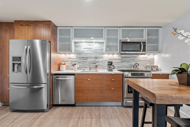 kitchen with light countertops, appliances with stainless steel finishes, backsplash, brown cabinets, and glass insert cabinets